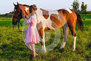 Beautiful girl in pink dress with horse in the field