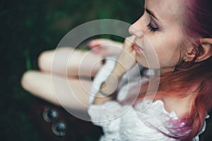 The beautiful girl with pink hair sits on the thrown ladder in an environment of a green grass