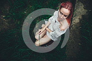 The beautiful girl with pink hair sits on the thrown ladder in an environment of a green grass