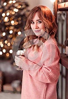 Beautiful girl in a pink sweater with a cup of coffee and marshmallows in hands on a background of New Year  lights