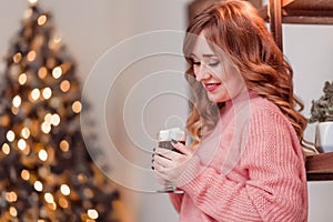Beautiful girl in a pink sweater with a cup of coffee and marshmallows in hands on a background of New Year  lights