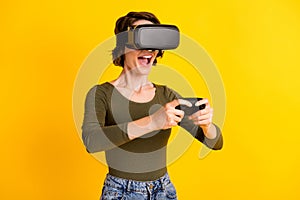 Beautiful girl play video game with joystick in vr goggles wear green denim sweater isolated on shine yellow color