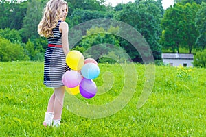 Beautiful girl playing with colorful balloons in the summer day against the blue sky