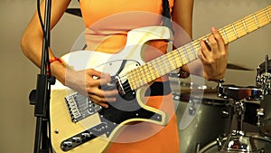 Beautiful girl plays the electric guitar. Musician in a bright orange dress. Designer stringed musical instrument of light color.