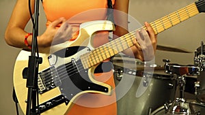 Beautiful girl plays the electric guitar. Musician in a bright orange dress. Designer stringed musical instrument of light color.