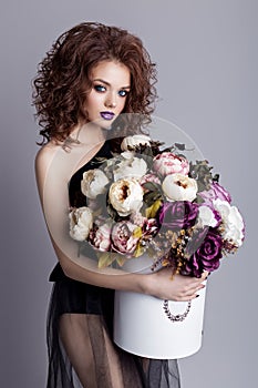 Beautiful girl with plump lips in black body with a bouquet of flowers in the studio, evening hairstyle and makeup