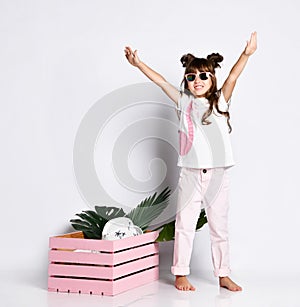 A beautiful girl poses next to a pink wooden box, wearing A Flamingo t-shirt and sunglasses, barefoot