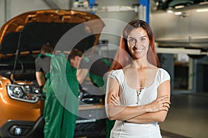 A beautiful girl poses for a photo while, two young mechanics in