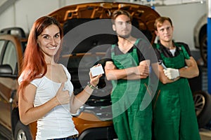 A beautiful girl poses for a photo while, two young mechanics in