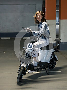 beautiful girl posing sitting on an electric scooter in the parking lot photo