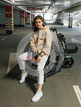 beautiful girl posing sitting on an electric scooter in the parking lot photo