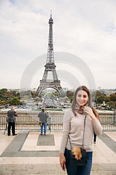 Beautiful girl posing to the photographer against the background of the Eiffel Tower. Autumn photosession. Sunny weather