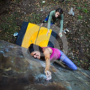 A beautiful girl practicing bouldering passes with the crash pad