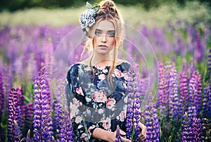 Beautiful girl in a purple lupin field with a flower on her head made of genuine leather and silk. Outdoor portrait