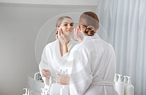 Beautiful girl putting cream on her face in bathroom