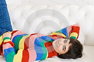 Beautiful girl in rainbow sweater lies on white sofa