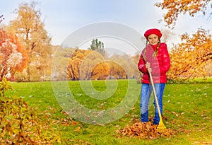 Beautiful girl with rake cleans grass from leaves