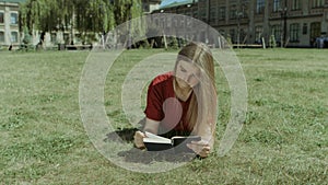 Beautiful girl reading a book on campus lawn