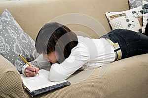 Beautiful girl reading a book lying on tan sofa