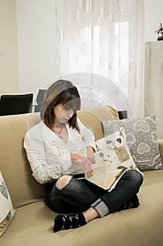 Beautiful girl reading a book sitting on tan sofa