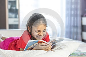 Beautiful girl reading book and smiling. Girl wearing red T-shirt, studying at home with books and doing school homework. Smiling