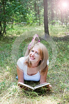 Beautiful girl reading lying on the grass in the forest whith l