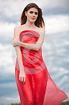 Beautiful girl in a red cape on the summer meadow