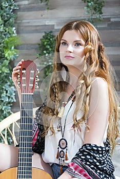 A beautiful girl with red curly hair sits on a chair with a seven-string guitar.