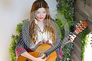 A beautiful girl with red curly hair stands and holds a seven-string guitar in her hands.