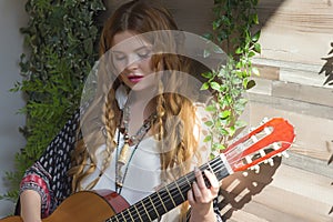 A beautiful girl with red curly hair stands and holds a seven-string guitar in her hands.