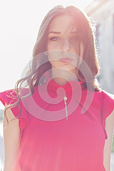 Beautiful girl in a red dress with a gentle look into the sun at sunset in bright sunny day