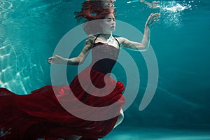 Beautiful girl in a red dress swims under water. amazing Underwater