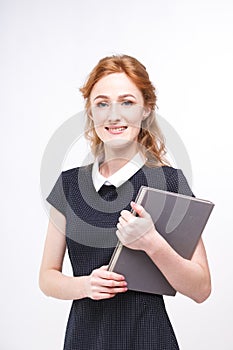 Beautiful girl with red hair and gray book in hands dressed in black dress white isolated background