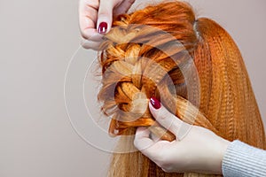 Beautiful girl with red hair, hairdresser weaves a braid close-up, in a beauty salon.