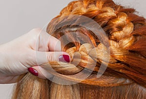 Beautiful girl with red hair, hairdresser weaves a braid close-up, in a beauty salon