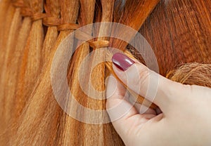 Beautiful girl with red hair, hairdresser weaves a braid close-up, in a beauty salon