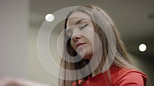 Beautiful girl in red shirt and blue leggins pedals on the exercise bike and watchs time in the new gym