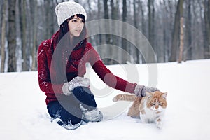 Beautiful girl with in red sweater and hat holding and playing with little fluffy cat in winter snowy park. Pets, comfort, christm