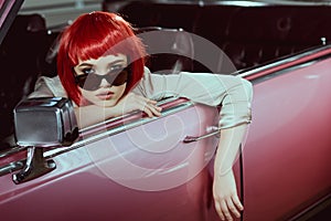 beautiful girl in red wig and sunglasses sitting in retro car and looking