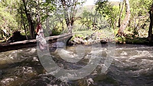 A beautiful girl relaxes by the lake, sitting on the edge of a wooden bridge, swinging her feet at the surface of the