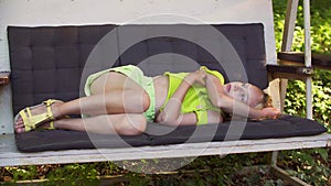 Beautiful girl relaxing in garden swing in summer countryside. Dreaming girl lying on swing sofa in summer garden on
