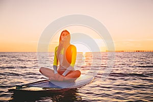 Beautiful girl relaxing on stand up paddle board, on a quiet sea with warm sunset colors.