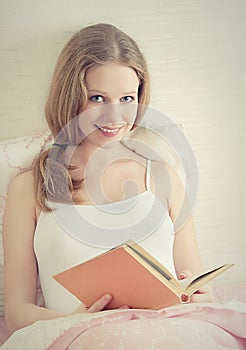 Beautiful girl is resting in bed, reading book