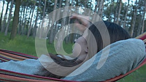 A beautiful girl is resting in the park on a hammock. Young woman lying in a hammock in garden