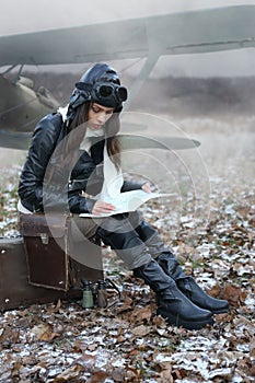 Beautiful girl in a retro aviator costume looking at the map