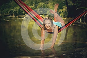 Beautiful girl riding in a hammock over the water.