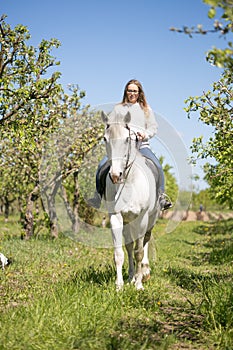 Beautiful girl riding a horse on a white horse in the garden