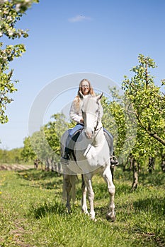 Beautiful girl riding a horse on a white horse in the garden