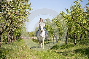 Beautiful girl riding a horse on a white horse in the garden