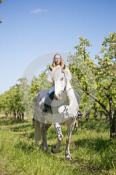 Beautiful girl riding a horse on a white horse in the garden